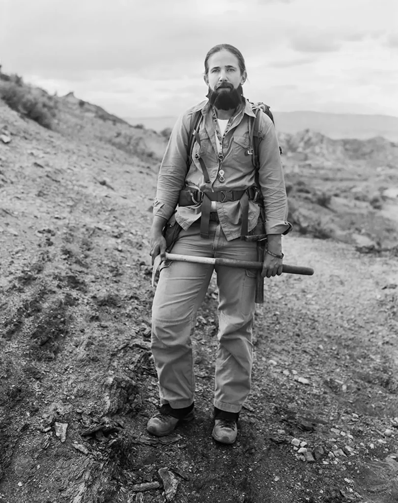 Black and white photography of Ellen Currano at ab arechological dig site, wearing a beard.