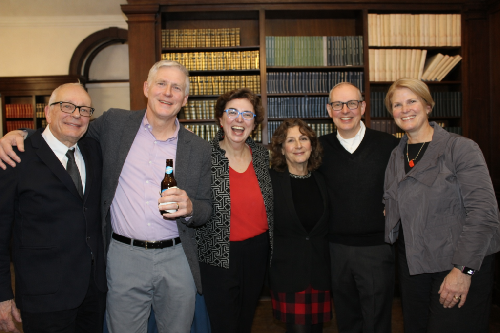 A photo of a group of six people in front of a book case facing forward and smiling.